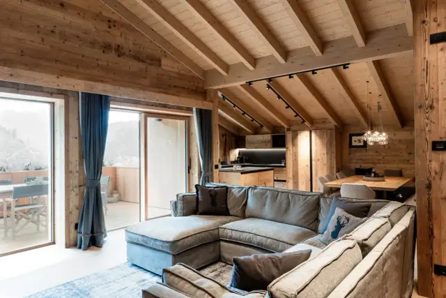 Cozy mountain chalet living room with sectional sofa, wooden beams, and large windows.