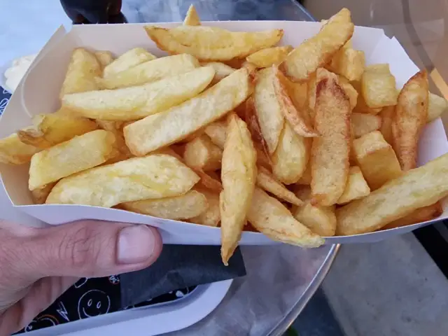 Złociste, chrupiące frytki w papierowym opakowaniu, trzymane w dłoni.