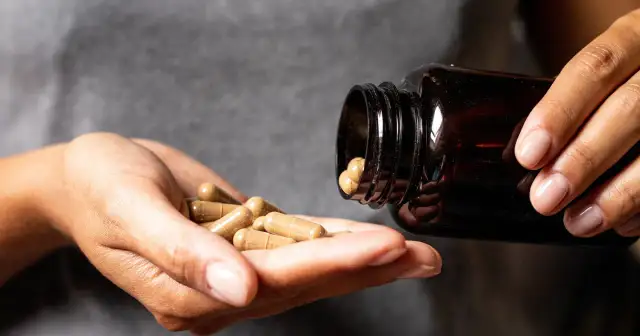 Dłonie wysypują kapsułki z brązowej buteleczki. Czy ashwagandha uzależnia? To pytanie nurtuje wiele osób szukających naturalnych sposobów na poprawę samopoczucia.