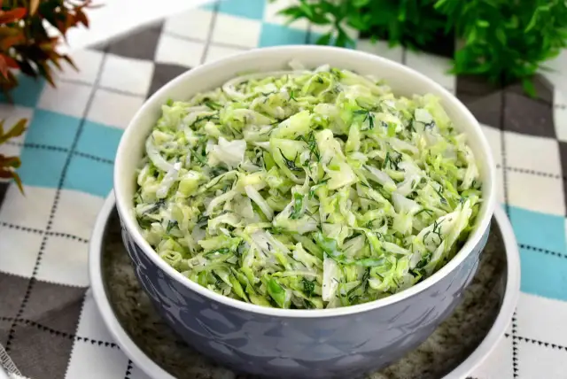 Pyszna surówka z białej kapusty z koperkiem, podana w szarej misce na wzorzystym obrusie.