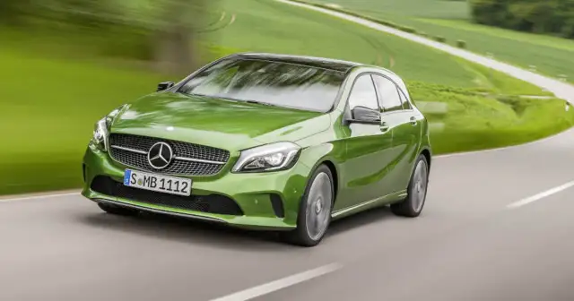 Zielony Mercedes klasy C pędzi po krętej drodze wśród zielonych pól.