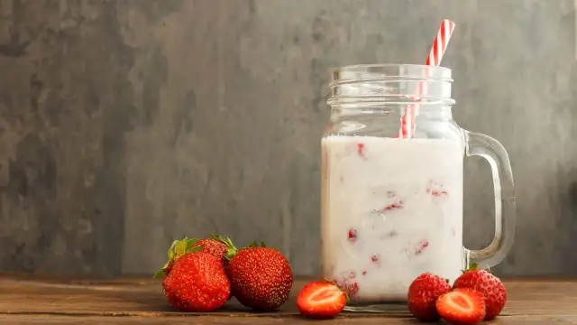 Kefir z truskawkami w słoiku, obok świeże owoce. Niska wartość indeksu glikemicznego sprawia, że to zdrowa przekąska.