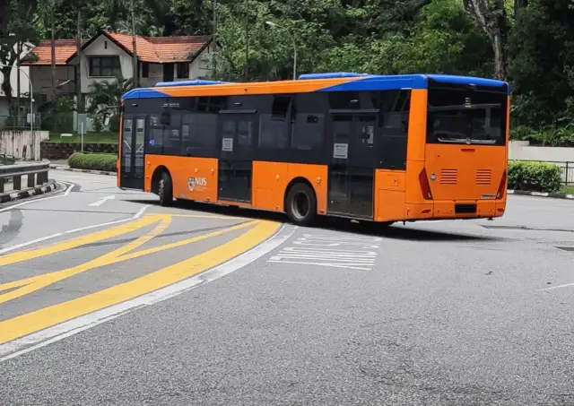 Pomarańczowo-niebieski autobus miejski na zakręcie drogi z żółtymi pasami.