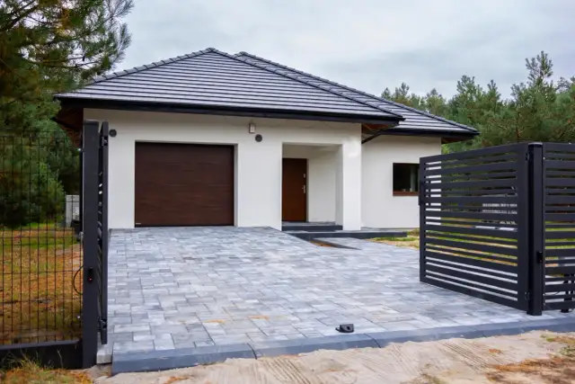 Nowoczesny dom z garażem, podjazd z kostki brukowej, czarna brama. Kubatura domu 100m2.