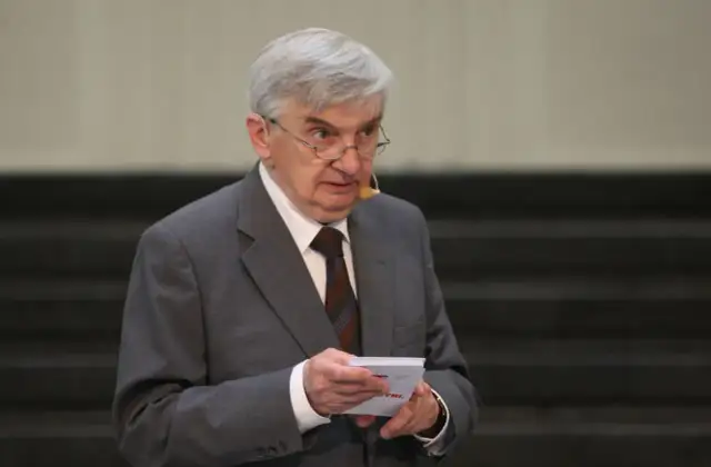 Starszy mężczyzna w garniturze, który prowadzi jeden z dziesięciu, trzyma kartkę.