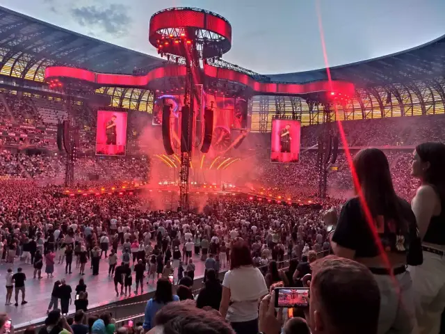 Koncert Dawida Podsiadło na stadionie, tłum ludzi, scena z czerwonymi światłami i ekranami.