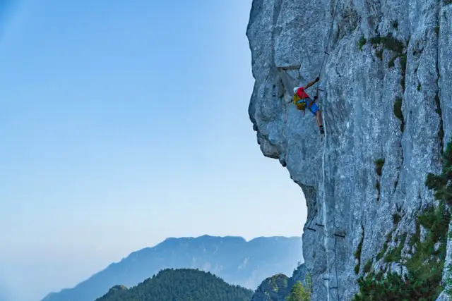 Wspinacz pokonuje via ferrata niemcy, zmagając się z pionową ścianą skalną. W tle piękne góry.