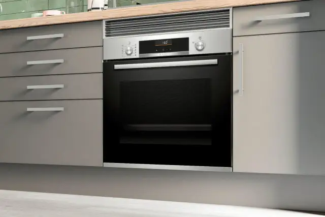 Moderno horno integrado en una cocina con cajones grises y encimera de madera.