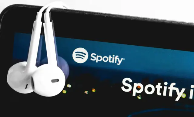 Białe słuchawki wiszą na ekranie smartfona z logo Spotify.