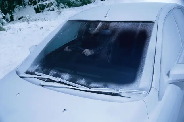 Zamarznięta przednia szyba samochodu. Kierowca w środku, przygotowuje się do uruchomienia podgrzewania przedniej szyby, by ruszyć w mroźny dzień.