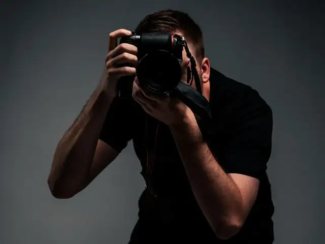 Mężczyzna w czarnej koszulce trzyma aparat fotograficzny i robi zdjęcie.