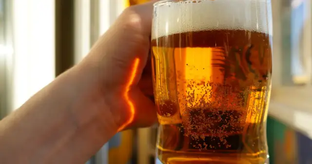 Dłoń trzymająca szklankę złocistego piwa z pianką i bąbelkami.