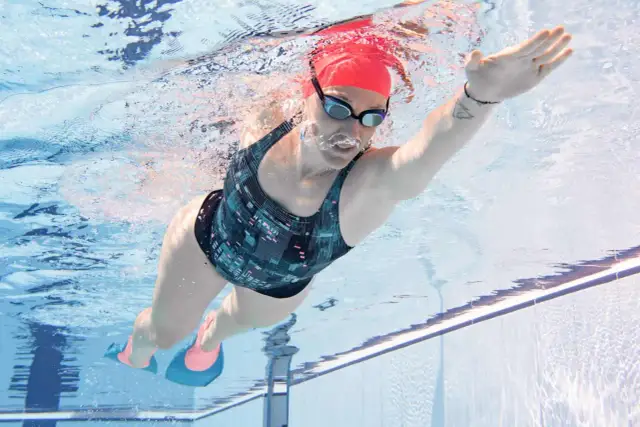 Kobieta w czerwnym czepku i okularach pływa kraulem, używając płetw.