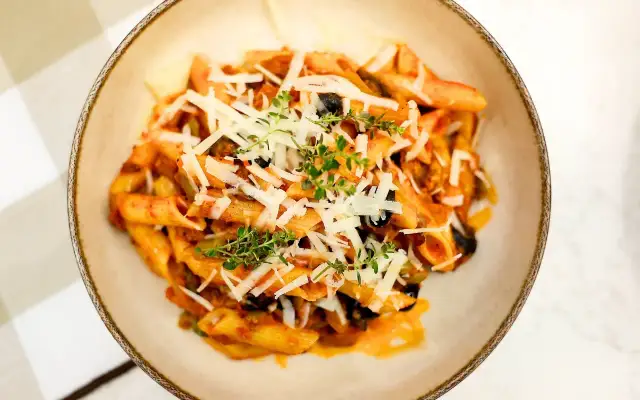 Penne z bogatym sosem anchois, czarnymi oliwkami i parmezanem, udekorowane świeżym tymiankiem.