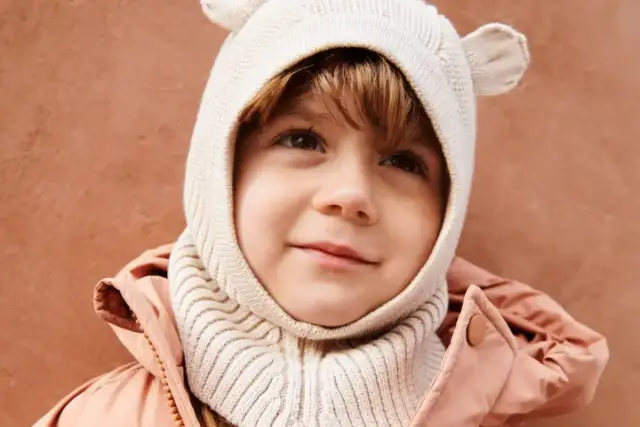 Uśmiechnięte dziecko w beżowej czapce z uszkami i różowej kurtce.
