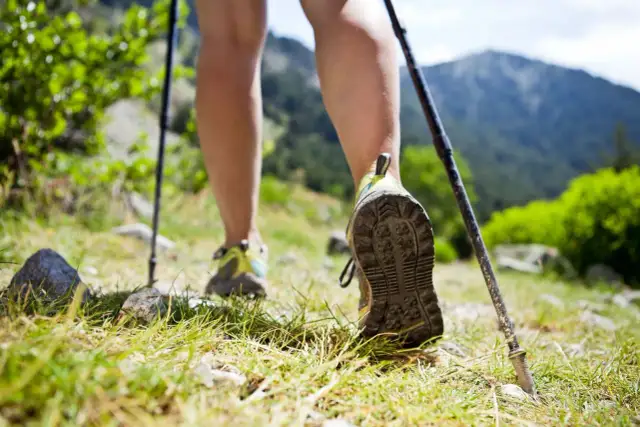 Naucz się, jak chodzić z kijkami, by czerpać radość z górskich wędrówek. Nogi w butach trekkingowych i kijki na trawiastym szlaku.