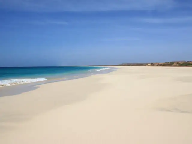 Pusta, piaszczysta plaża z turkusową wodą i błękitnym niebem.