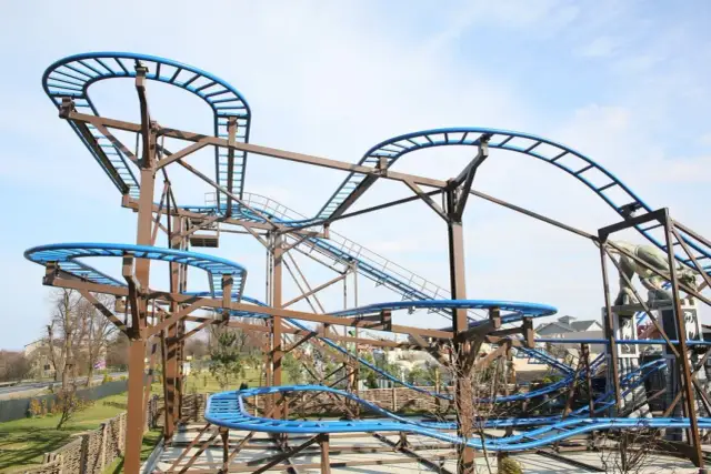 Tor kolejki górskiej z niebieskimi szynami i brązową konstrukcją na tle nieba.