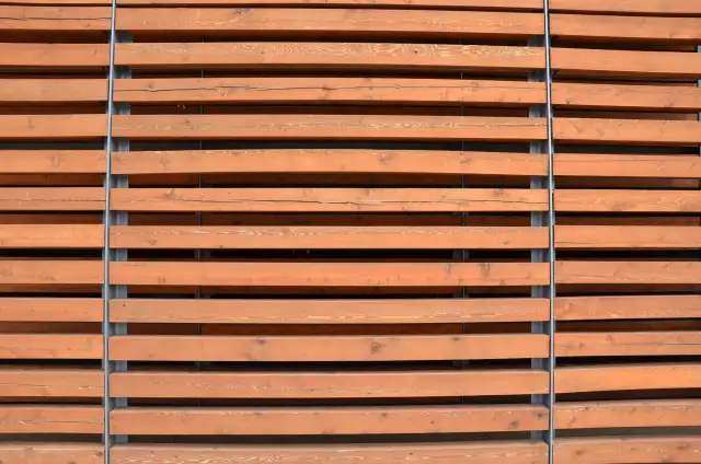 Drewniane lamele ścienne w kolorze miodowym, ułożone poziomo i przymocowane do szarych słupków.