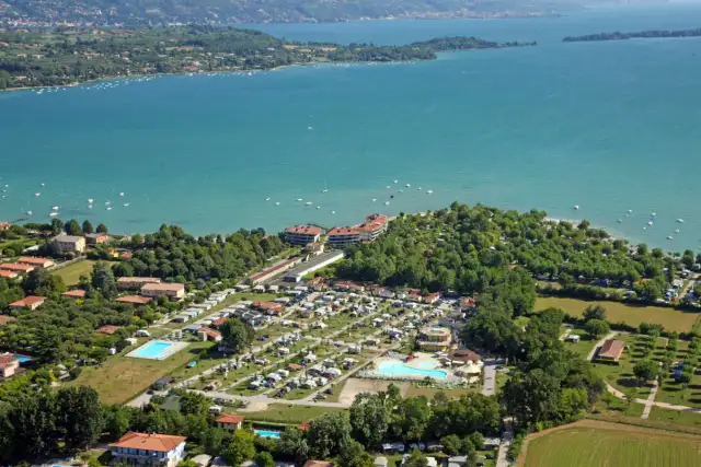 Widok z lotu ptaka na camping Baia Verde nad turkusowym jeziorem, z basenami i licznymi namiotami.