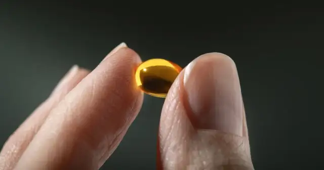 Dłoń trzymająca złotą kapsułkę z witaminą D.