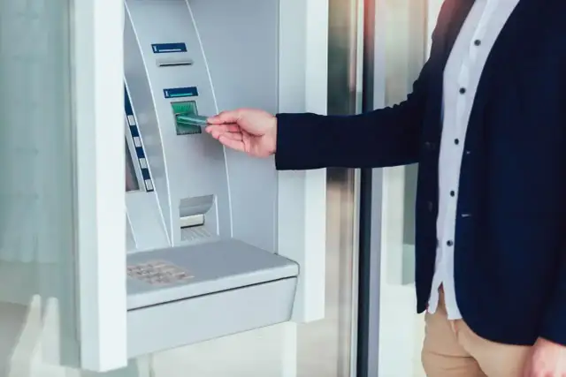 Mężczyzna w garniturze wkłada kartę do wpłatomatu euro. Szybka transakcja w bankomacie.