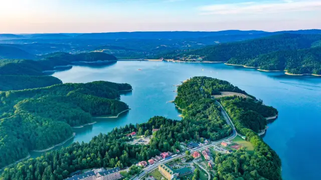 Widok z lotu ptaka na jezioro otoczone lasami, z widocznymi zabudowaniami i zaporą.