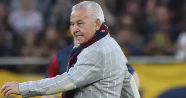 Starszy pan w marynarce w kratę i szaliku, przypominający zmarłego wczoraj piłkarza, na tle tłumu.