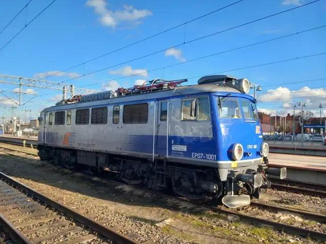 Niebiesko-szara lokomotywa PKP Intercity EP07-1001 na torach kolejowych.