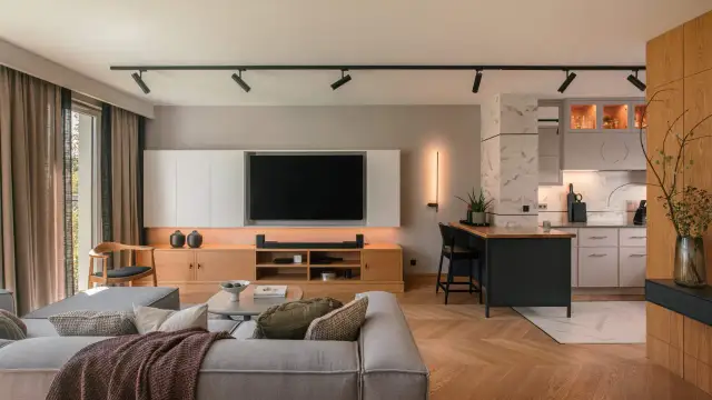 Nowoczesny salon z aneksem kuchennym, gdzie każdy detal tworzy elegancki dom. Drewniana podłoga w jodełkę, szara sofa i wyspa kuchenna.