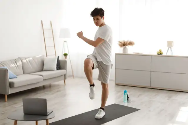 Młody mężczyzna ćwiczy bieganie w miejscu na macie w salonie.