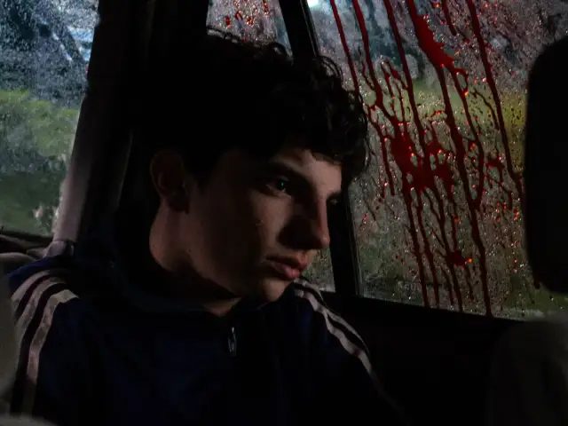 Młody chłopak w samochodzie, patrzący na ślady krwi na szybie. Czuć, gdy rodzi się zło.