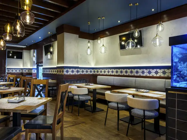 Wnętrze restauracji z drewnianymi stołami, krzesłami i ozdobnymi lampami.