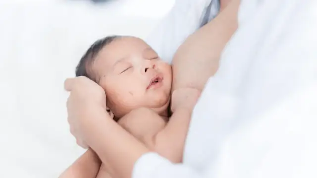 Niemowlę pręży się i wygina podczas karmienia, wtulone w ramiona mamy.