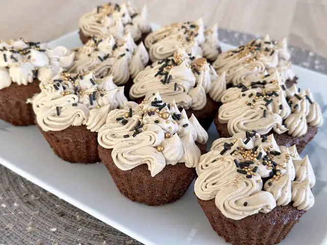 Czekoladowe babeczki z kremem i złotymi oraz czarnymi posypkami na białym talerzu.