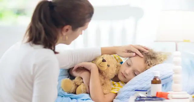 Matka czule głaszcze śpiące dziecko z misiem. Zastanawia się, ile trwa kaszel u dziecka i czy potrzebna jest kolejna wizyta u lekarza.