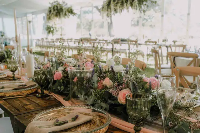 Stół weselny z bukietem różowych i białych kwiatów, zielonymi kieliszkami i świecami.