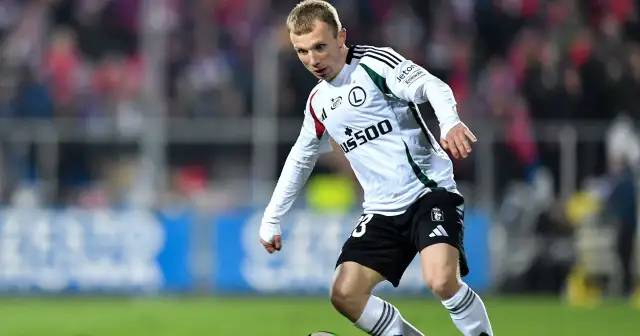 Piłkarz Legii Warszawa w białej koszulce i czarnych spodenkach biegnie z piłką.