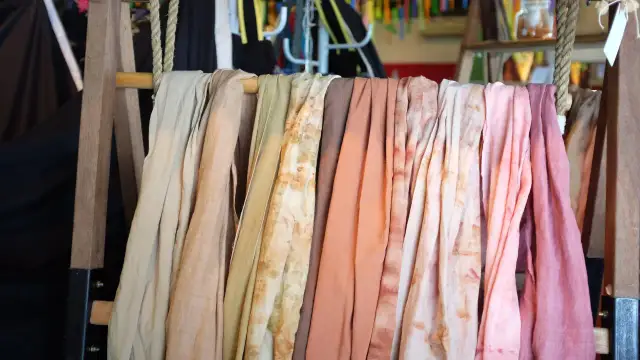 Rzędy tkanin w pastelowych kolorach, niektóre z plamami, wiszące na drewnianym stojaku.