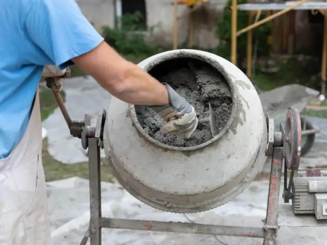 Mieszanie betonu w betoniarce. Pracownik w rękawicach sprawdza konsystencję, zastanawiając się, ile cementu na metr sześcienny betonu potrzeba do uzyskania idealnej mieszanki.