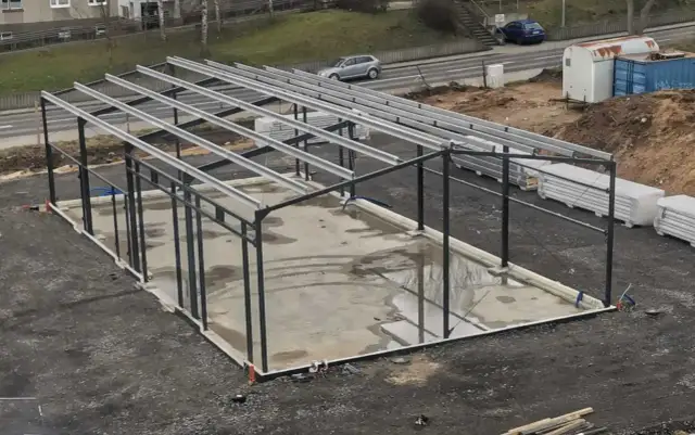 Budowa hali stalowej. Zastanawiasz się, ile kosztuje 1 kg konstrukcji stalowej? Na placu budowy widać szkielet hali i materiały budowlane.