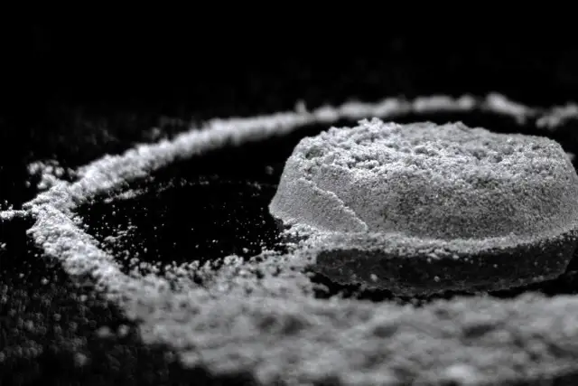 Biały proszek uformowany w kopczyk i linię na czarnym tle.