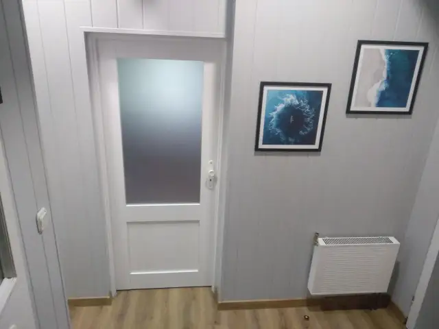 Biała boazeria w przedpokoju z drzwiami i obrazami o tematyce morskiej.