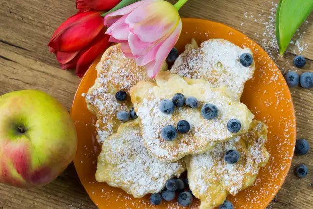 Pyszne, puszyste placuszki posypane cukrem pudrem i borówkami. Idealne dania bezglutenowe przepisy na śniadanie. Obok jabłko i tulipany.