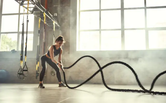 Kobieta ćwiczy z linami treningowymi, pokazując, na czym polega trening crossfit: siła, wytrzymałość i dynamika.