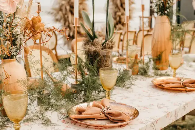 Stół weselny z kwiatami, świecami i złotymi naczyniami.