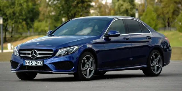 Granatowy Mercedes Klasy C, idealny do poznania jego **mercedes c klasa dane techniczne**. Elegancki sedan na tle zieleni.