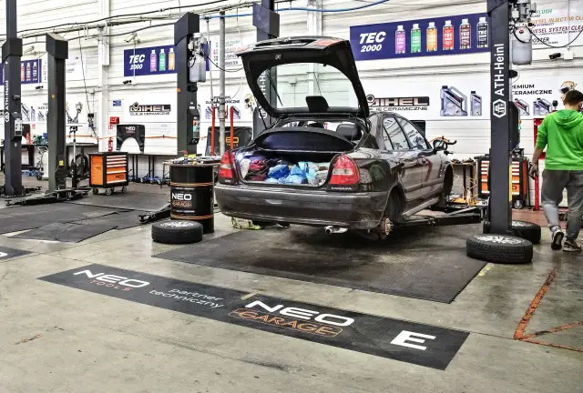 Warsztat samoobsługowy Warszawa: samochód na podnośniku, bagażnik otwarty, narzędzia i części widoczne.