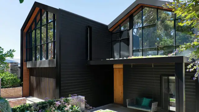 Nowoczesny czarny dom szkieletowy z dużymi oknami i zielonym dachem.