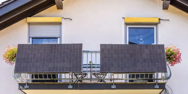 Dwa panele fotowoltaiczne na balkonie, symbolizujące odnawialne źródła energii w domu. Obok kwitnące kwiaty.